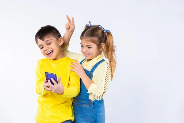 Pasatiempo y niños emociones en blanco. Los niños toman selfies en un teléfono inteligente y ponen cuernos. —  Fotos de Stock