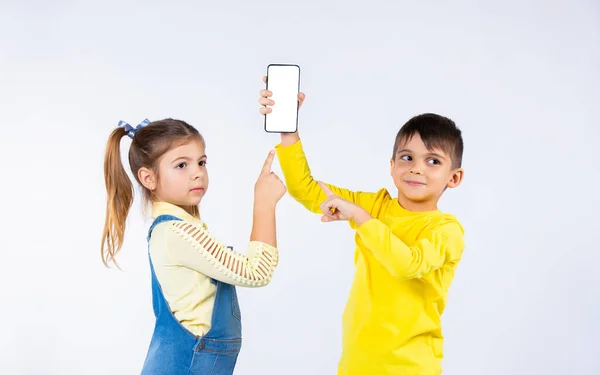 Niños en edad preescolar en un punto de fondo blanco con un dedo índice en la pantalla del teléfono inteligente y mirar a un lado. —  Fotos de Stock