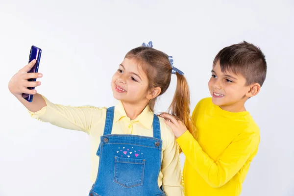 Les enfants d'âge préscolaire sourient et posent mignon tout en prenant selfie sur un smartphone. Fond blanc. — Photo