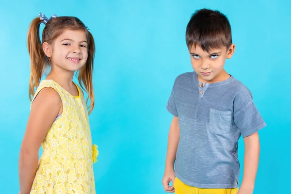 El concepto de emociones infantiles sobre un fondo azul. Chica sonriente y chico ofendido. — Foto de Stock