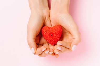Nazik manikürlü kadın elleri kalp şeklinde bir mum tutar. Pembe arka plan ve Sevgililer Günü konsepti.