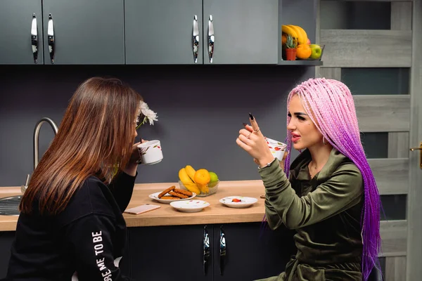 Mladé moderní dívky komunikují doma v kuchyni s šálkem kávy. Zábava přítelkyň.. — Stock fotografie
