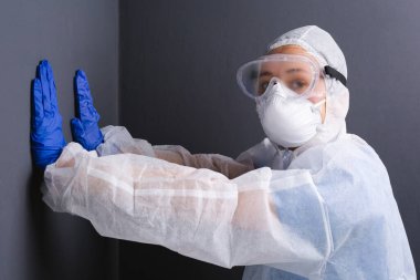 Üniformalı bir doktor ellerini gri bir duvara bastırıyor ve kameraya bakıyor. Koronavirüsle uğraşırken yorgunluk.