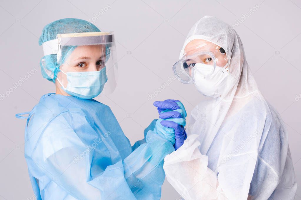 Pandemic. Tired doctors in covid-19 protective gear hold hands in support of a dire situation. Gray background.