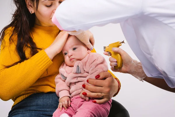 Foto ampliada. Las manos de los médicos están haciendo agujeros en las orejas con una pistola para un bebé. — Foto de Stock