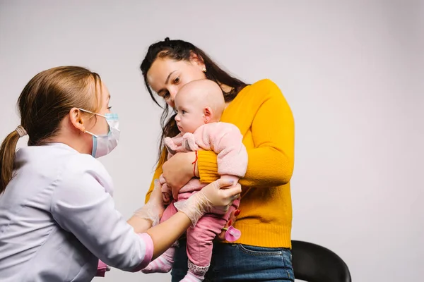 Una joven madre sostiene al bebé en sus brazos y el médico la anima antes del procedimiento sobre un fondo gris. — Foto de Stock