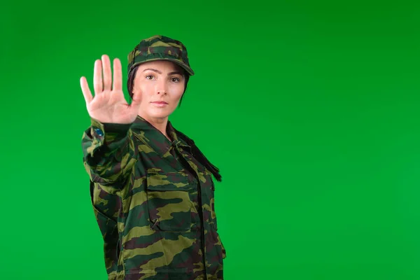 Una joven con un uniforme militar sobre un fondo verde muestra la parada a la cámara con espacio lateral en blanco. Detener la pandemia de soldado femenino — Foto de Stock