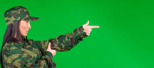 Banner de formato largo. Foto de perfil de una mujer en uniforme militar imita un arma o arma con las manos y mira hacia otro lado. Fondo verde. Igualdad de género sin miedo. — Foto de Stock