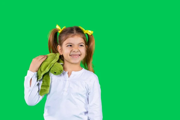 Menina pré-escolar feliz segurando uma tartaruga verde em seu ombro sorrindo e olhando para o lado em um fundo verde com espaço lateral. — Fotografia de Stock