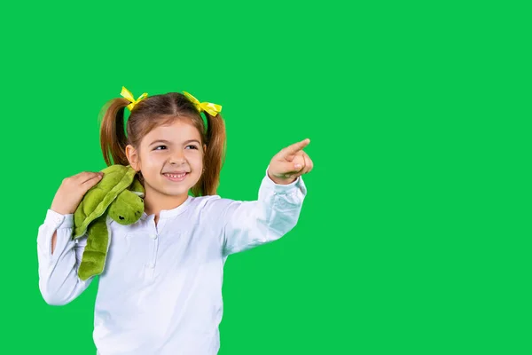 Une fille d'âge préscolaire avec une tortue verte sur l'épaule sourit et pointe son index sur le côté. — Photo