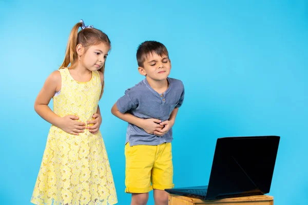 Los niños en edad preescolar se quejan de dolor abdominal delante de una computadora portátil. Fondo azul. —  Fotos de Stock