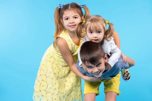 En grupp barn i olika åldrar leker och leker runt på en blå bakgrund med en tom sida utrymme. — Stockfoto