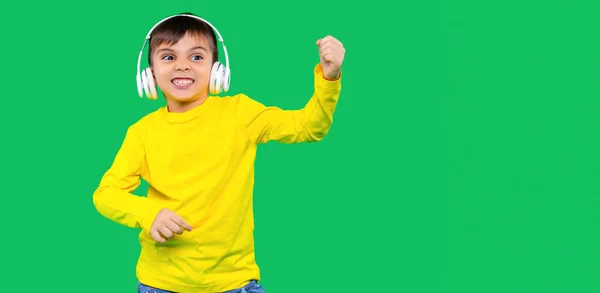 Banner. El chico escucha música en grandes auriculares y baila retorciéndose las caras sobre un fondo verde. — Foto de Stock