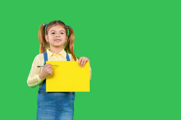 Το παιδί προσχολικής ηλικίας κρατά ένα φωτεινό πανό για διαφήμιση και δείχνει σε αυτό με ένα μολύβι. Πράσινο φόντο και πλευρικός χώρος. — Φωτογραφία Αρχείου