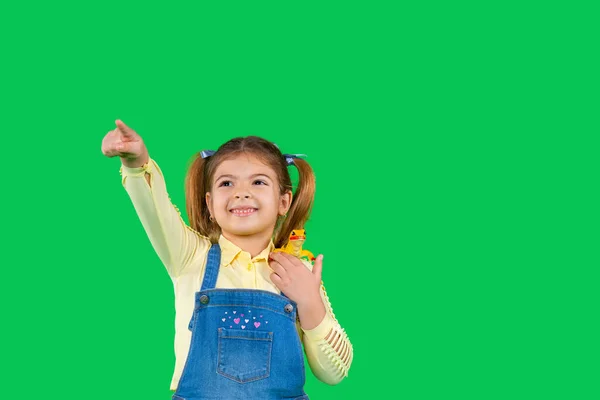 Uma pré-escolar segura um lagarto no ombro e aponta para a frente com o dedo indicador. Fundo verde com espaço lateral — Fotografia de Stock