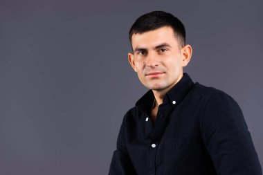 Siyah tişörtlü, gri arka planda, boş bir kenarı olan çekici bir gencin portresi..
