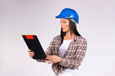 Mavi kasklı kadın müteahhit planı dikkatle okuyor. Yan alanı ve cinsiyet eşitliği olan gri arkaplan mühendisi.