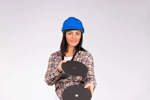 Joven morena de sombrero duro posando con discos abrasivos sobre un fondo blanco. El concepto de estereotipos de género. — Foto de Stock