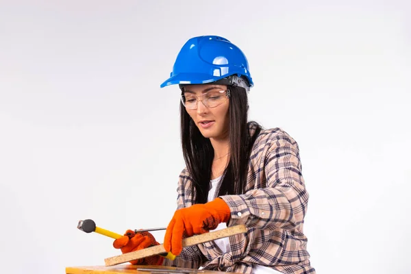 Woman in hard hat with hammer and nails is focused on work. White background.