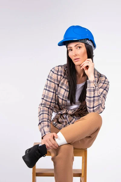 Retrato de una joven reparadora confiada en un hardhat constructor azul posando mirando a la cámara sobre un fondo gris. El concepto de igualdad de género. — Foto de Stock