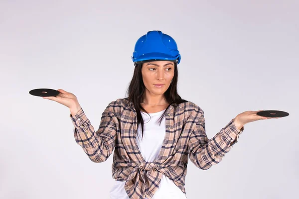 Una mujer con un sombrero duro con los brazos extendidos mira hacia un lado y sostiene discos abrasivos sobre un fondo blanco. — Foto de Stock