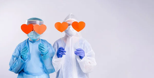 Pankart. Koruyucu ekipmandaki sağlık görevlileri kırmızı kalpleri kapalı tutarlar. Sevgililer günü, hayır kurumu ve insan destek konsepti. Beyaz arka plan. Boş kenar boşluk.
