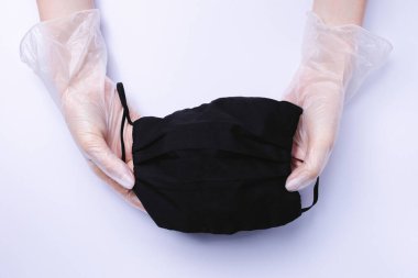 Eldivenli kadın eller beyaz arka planda siyah bir tıbbi maske takıyor..
