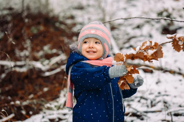 Bonne petite fille chaudement habillée joue dans un parc d'hiver et regarde de côté. — Photo