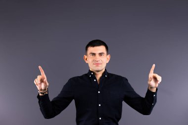 Modaya uygun bir adam kameraya bakar ve işaret parmaklarını gri bir arka planda gösterir..