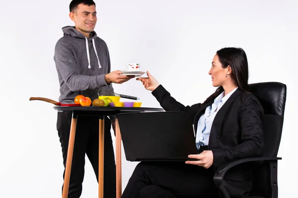 Uma mulher trabalha num computador. Um homem cuida dela, serve café num fundo branco.. — Fotografia de Stock