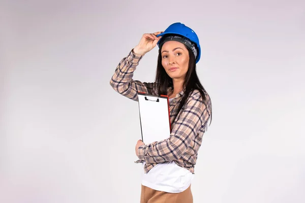 Mujer joven ingeniero con una carpeta de documentos se aferra a un sombrero duro azul y mira a la cámara sobre un fondo blanco. — Foto de Stock