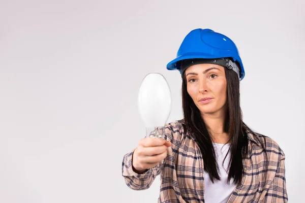 Uma mulher séria com um chapéu azul dura segura uma mão frontal em direção à lâmpada LED da câmera em um fundo branco com espaço lateral vazio. — Fotografia de Stock