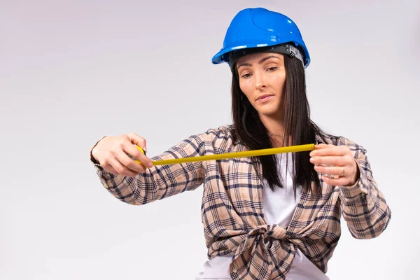 En ung kvinna i blå hatt tittar på ett måttband i händerna. Vit bakgrund. — Stockfoto