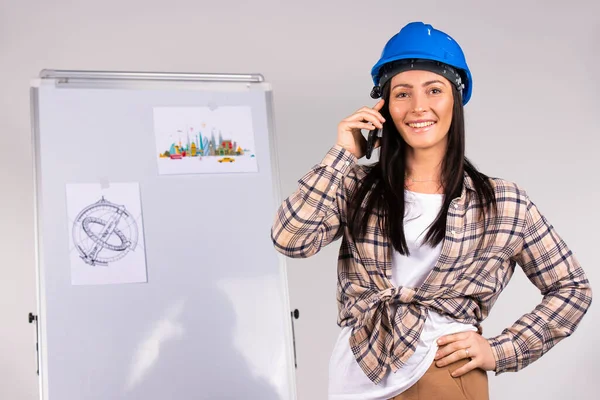 Uma arquiteta está falando ao telefone e sorrindo para a câmera contra o pano de fundo de um projeto de escritório. Estereótipos de género. — Fotografia de Stock