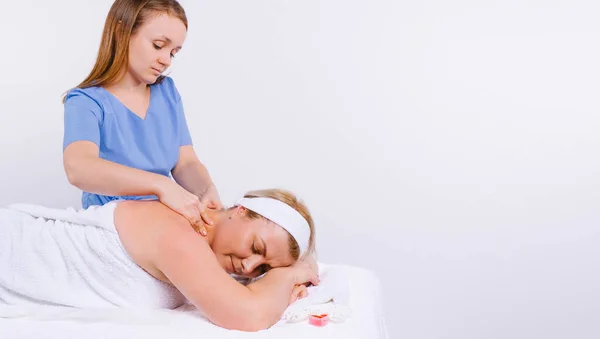 Bandiera. Il giovane massaggiatore maestro fa un massaggio su uno sfondo bianco a una donna nel salone con candele profumate. Spazio laterale. — Foto Stock
