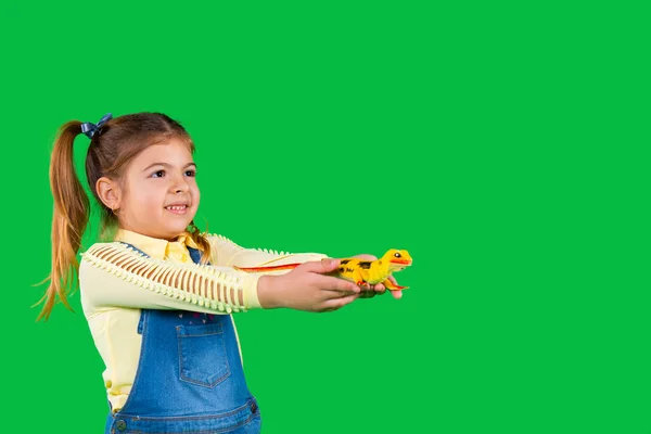 Uma menina da criança olha para o lado e segura um lagarto doméstico em um fundo verde com espaço lateral para o seu anúncio — Fotografia de Stock