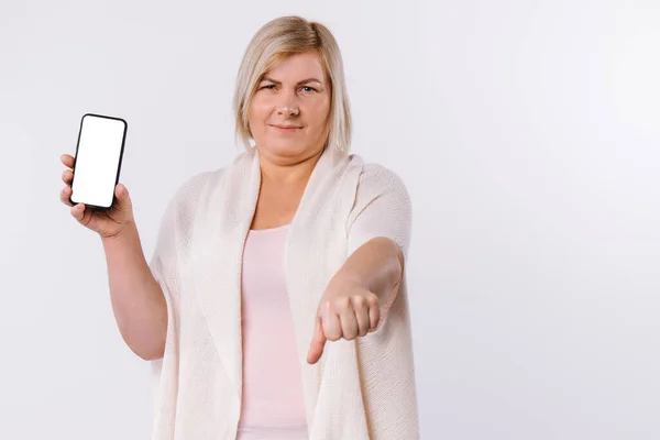 Mujer caucásica insatisfecha está mostrando una pantalla de teléfono y con la otra mano un signo de aversión. Pulgar hacia abajo sobre un fondo blanco. —  Fotos de Stock