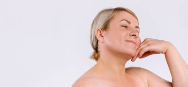 Pankart. Kozmetik ameliyatlardan sonra nemlendirilmiş cilde sahip yaşlı bir kadın gülümser ve yüzüne nazikçe bakar. Boş alana sahip beyaz arkaplan.