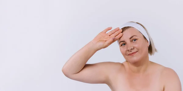 Bannière. Une femme plus âgée dans un pansement blanc et une peau hydratée après les procédures à la maison regarde dans une caméra sur un fond gris. — Photo