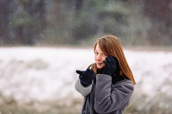 Une jolie fille d'apparence caucasienne parle au téléphone et regarde la caméra sur un fond neigeux. — Photo