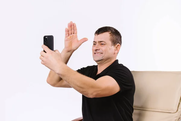 Happy senior man communicates non-verbally via video dialogue while sitting home in a chair on a white background. Online work in pandemic — Stock Photo, Image