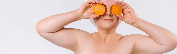 Банер, довгий формат. Розширене фото старшої жінки, що тримає помаранчеві скибочки на білому тлі з порожнім бічним рекламним простором . — стокове фото