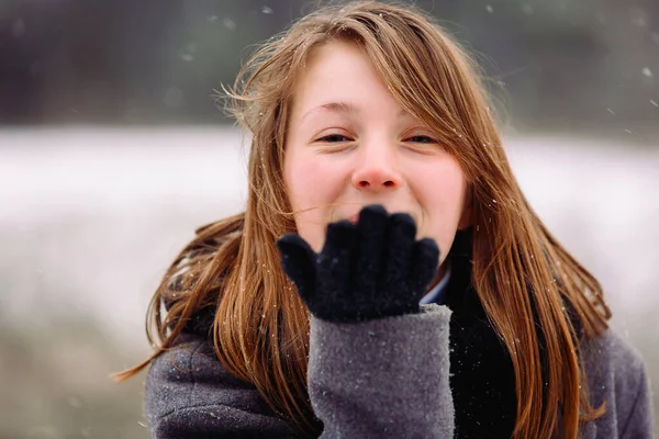 Uma foto ampliada de uma jovem garota soprando um beijo na câmera. Foto contra o pano de fundo da paisagem coberta de neve. — Fotografia de Stock