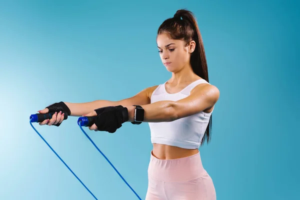 Egy női sportoló portréja gyakorlatok közben, ugrókötéllel a kék háttéren. Egészséges életmód koncepció. — Stock Fotó