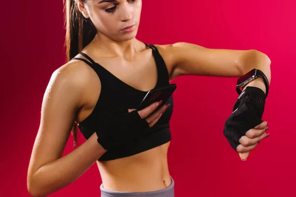 Detailní záběr zaostřené brunetky s fitness trackerem a smartphonem na červeném pozadí. Zdravotní život s Smartwatch — Stock fotografie
