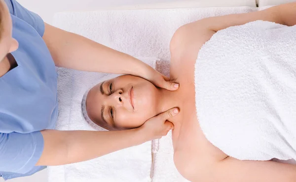 De meester masseur geeft een ontspannende hoofd-halsmassage aan een oudere vrouw gewikkeld in een witte handdoek. — Stockfoto