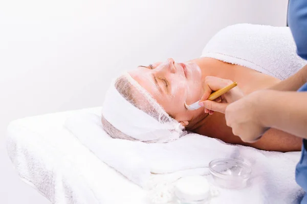 Enlarged photo. The beautician applies a moisturizing mask to the face of an older woman with a brush. — Stock Photo, Image