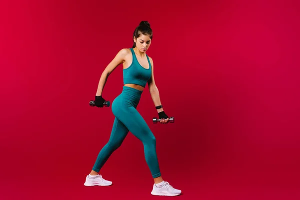 Sportovní svalnatá brunetka s činkami na červeném pozadí s prázdným bočním reklamním prostorem. Sportovní koncept. — Stock fotografie