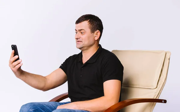 Ανώτερος άνθρωπος με προβλήματα ακοής κάθεται σε μια δερμάτινη καρέκλα γραφείου και επικοινωνεί μέσω βίντεο επικοινωνίας στο τηλέφωνο. Λευκό φόντο. — Φωτογραφία Αρχείου