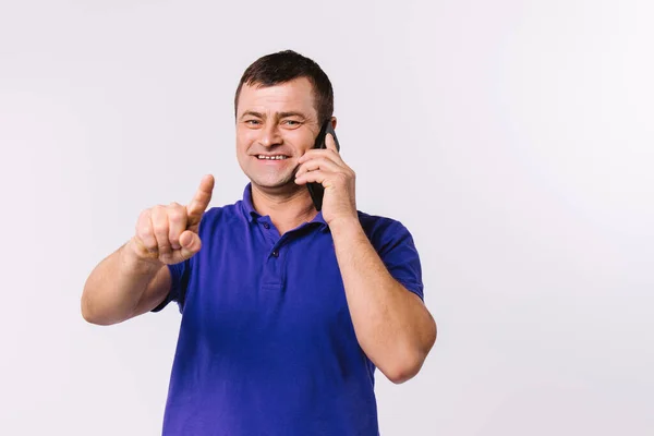 Καυκάσιος άντρας με καθημερινά ρούχα να μιλάει στο τηλέφωνο και να δείχνει με τον δείκτη του πάνω σε λευκό φόντο και να χαμογελάει.. — Φωτογραφία Αρχείου